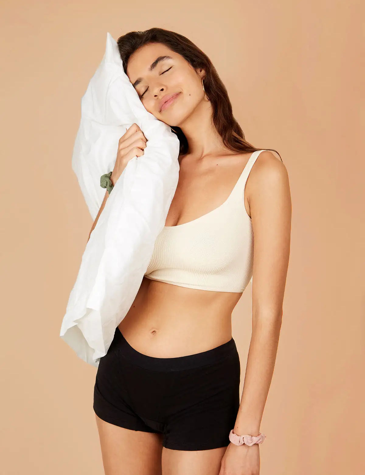 Woman wearing boxer-style sleep shorts, holding a pillow to her head, looking relaxed.